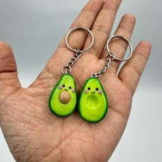 two green avocado shaped key chains in the palm of a person's hand