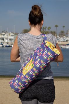 a woman carrying a large duffel bag on the beach with boats in the background