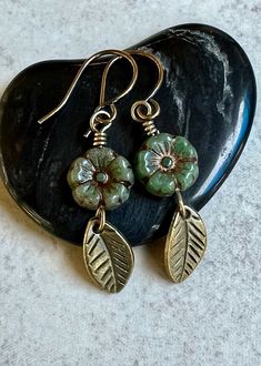 two leaf shaped earrings with green beads and gold accents on a black heart - shaped rock