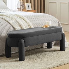 a gray bench sitting on top of a rug in a bedroom next to a bed