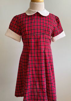 "This dress has a very prim and proper look to it and is just incredibly charming when worn. Made at home without a label, the fabric is a cotton dobby with a red ground and a black and white check pattern woven into it. The front bodice is high and shaped by the tiniest of pleats. The skirt is straight through midriff, then gored (A-line panels seamed together). This gives a nipped in waist and very twirly skirt look to the dress. Sleeves are short with just the hint of a gather at crown. Cuffs Retro Short Sleeve School Dresses, Fitted Red Plaid Dress With Short Sleeves, Red Fitted Plaid Dress With Short Sleeves, Retro Fitted Dress For School, Retro Fitted School Dress, Retro Cotton Plaid Dress, Red Short Sleeve School Dress, Retro Plaid Cotton Dress, Vintage A-line Plaid Dress