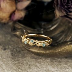 a gold ring with three blue stones on it and some flowers in the back ground