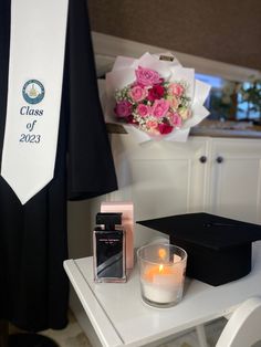 a candle and some flowers on a table with a graduation sash hanging in the background