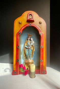 a small shrine with a candle and some flowers on the table in front of it