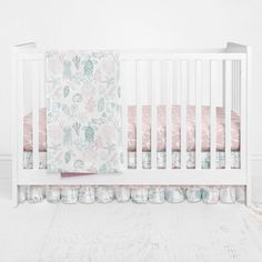 a white crib with pink and green bedding on it's bottom half