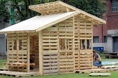 a small wooden building made out of wood pallets on the grass in front of a brick building