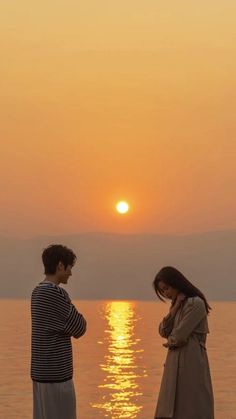 two people standing near the water at sunset