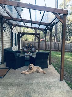 a dog laying on the ground under a pergolated covered patio with chairs and table