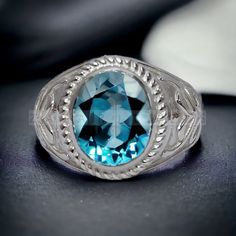 a ring with a blue topaz surrounded by silver filigrees on a black surface