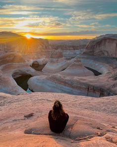 a woman sitting on top of a mountain looking at the sunset over canyons and cliffs