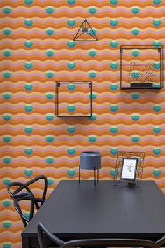 a dining room table with two chairs and a laptop on it, in front of a colorful wallpaper