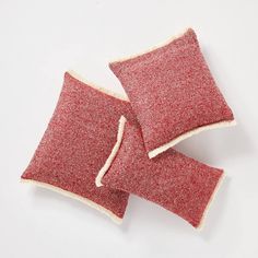 two red pillows sitting next to each other on top of a white surface with one pillow folded up