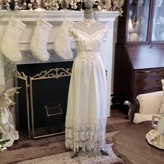 two white dresses are on display in front of a fireplace with stockings hanging from the mantel