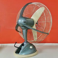 an old style fan sitting on top of a white table next to a red wall