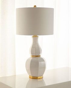 a white lamp sitting on top of a table next to a window with curtains behind it