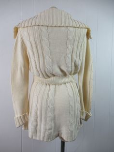 "Vintage 1970s sweater. Made of Acrylic knit. Color is cream white. Bohemian hippy style. Has a button down front, wooden buttons, large cowl style collar, internal cinches waist belt and two lower pockets. Made by F.O.B./ N.Y. About a size medium. Actual measurements are: 36\" at the bust 29\" at the waist 39\" at the hips 15.5\" shoulder seam to shoulder seam 28\" shoulder seam to cuff(with cuffs not rolled up) 33\" overall length In excellent condition." Vintage Knit Sweater Coat With Long Sleeves, Vintage Knit Sweater Coat, Vintage Knitted Sweater Coat With Long Sleeves, Vintage Knitted Long Sleeve Sweater Coat, Long Fitted Cream Sweater, Fitted Vintage Sweater Coat With Long Sleeves, Fitted Long Sleeve Vintage Sweater Coat, Vintage Cream Long Sleeve Sweater, Vintage Cream Cable Knit Cardigan