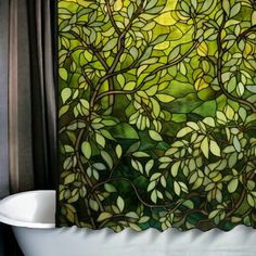 a bath tub sitting under a window next to a shower curtain with leaves on it