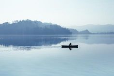 a person in a canoe paddling on the water with mountains in the background and foggy sky