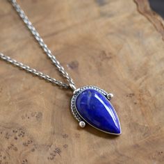 a necklace with a blue stone on it sitting on top of a piece of wood