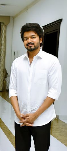 a man in white shirt and black pants standing in front of a door with his hands on his hips