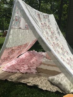 a tent that is sitting in the grass with pink sheets on it and some pillows