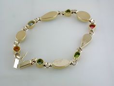 Ethiopian opals, topaz, tanzanite, citrine, peridot, tourmaline, green diopsite of various shapes and sizes are each delicately set in handmade bezels. This 14k yellow gold bracelet has been hand signed by the artist. 14K Yellow Gold & 22K Yellow Gold Ethiopian opals, topaz, tanzanite, citrine, peridot, tourmaline, green diopsite 7 1/4" long Plunger Clasp with figure 8 safety 9mm at widest point Weighs approximately 8.4 grams Hand Signed Available for Order. (Orders Placed today will ship in Fusion Style Multi-stone Yellow Gold Gemstones, Yellow Gold Multi-stone Fusion Gemstones, Gold Multi-stone Fusion Gemstones, Gold Oval Fusion Gemstones, Heirloom Gold Multi-stone Bracelets, Oval Gold Fusion Gemstones, Heirloom Gold Bracelets With Multi-stone, Heirloom Yellow Gold Multi-stone Bracelets, Multi-stone Tourmaline Gemstones