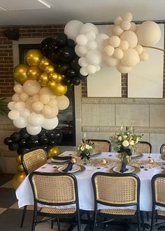 a dining room table set up for a party with white and gold balloons hanging from the ceiling