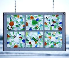 a stained glass window hanging from a chain on the beach with seagulls in the background