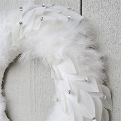 a white feather wreath hanging on the side of a door with silver beads and pearls