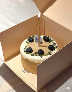 a birthday cake with two candles on it in a cardboard box that is open to show the inside