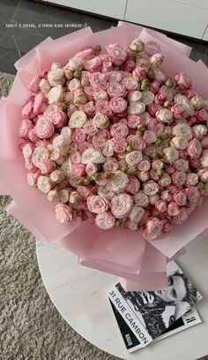 a large bouquet of pink and white roses on top of a coffee table in front of a magazine