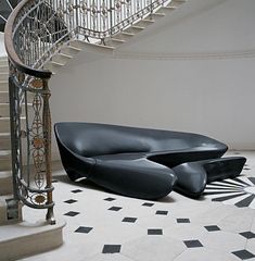 a black couch sitting in front of a spiral stair case on top of a tiled floor