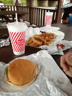 a hamburger and french fries are sitting on the picnic table with two cups of soda