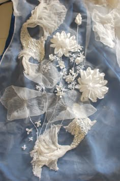 some white flowers and leaves on a blue cloth with sheer fabric around them, sitting on a table