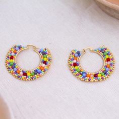 An avalanche of sizzling colors will dress your ears in style with these spectacular hoop earrings hand-crafted by artisan Adriana Trejo in Mexico. She threads multicolored glass beads onto a nylon cord and places them in a 14k gold-plated brass base for a pair of earrings that automatically makes your outfits come alive. Beaded Hoop Earrings Tutorial, Hoop Earrings Tutorial, Ad Earrings, Dramatic Earrings, Handmade Jewelry Tutorials, Artisan Earrings, Earring Tutorial, Rainbow Earrings, Beaded Hoop Earrings