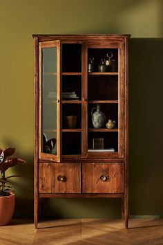 a wooden cabinet sitting on top of a hard wood floor next to a potted plant