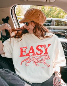 Add some retro vibes to your wardrobe with our vintage-inspired "Easy Tiger" graphic t-shirt! This trendy tee features a bold tiger design with a throwback to 70s vintage style, perfect for casual outfits, festival looks, or laid-back weekends. Made from soft, high-quality fabric, it offers both comfort and style, making it your go-to statement piece. Pair it with jeans, shorts, or a jacket for an effortlessly cool look. Available in a variety of sizes and colors, this graphic tee is perfect for Retro Slogan Tops, Trendy T-shirt With Vintage Print And Relaxed Fit, Retro Text Print T-shirt For Everyday, Retro Letter Print T-shirt For Everyday, Vintage Everyday T-shirt With Screen Print, Vintage Pre-shrunk T-shirt For Everyday, Vintage Letter Print T-shirt For Everyday, Retro Tops With Letter Print For Everyday, Retro Everyday Pre-shrunk T-shirt