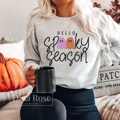 a woman sitting on a couch holding a coffee mug and wearing a sweatshirt that says hello lucky season