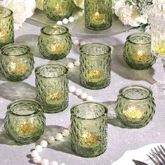 many green glass candles are sitting on a table with white flowers and beads around them