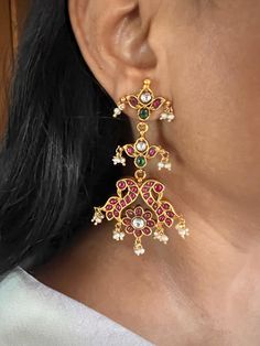 These stunning Kempu 925 silver earrings are meticulously handcrafted by fine jewelry artisans, featuring an elegant peacock design with natural freshwater pearl drops. Perfect for destination weddings and festive seasons like Navratras, these earrings combine traditional charm with intricate detailing, making them an ideal accessory for special occasions. Weight: 36 grams per pair Materials: 925 Silver, Kempu Stones, Freshwater Pearls, Gold Plated. Closure Type: Push Back Closure. Dimensions: Length is 7.5 cm and width is 4 cm. Designed to enhance your festive look, these earrings offer a perfect blend of comfort and sophistication. Festive Silver Pearl Earrings With Elegant Design, Elegant Peacock Design Chandelier Earrings For Festive Occasions, Elegant Festive Chandelier Earrings With Peacock Design, Elegant Peacock Design Chandelier Earrings, Elegant Earrings With Peacock Design For Gift, Elegant Peacock Design Dangle Earrings, Elegant Peacock Design Earrings As Gift, Elegant Dangle Earrings With Peacock Design, Elegant Peacock Design Bridal Earrings For Festive Occasion