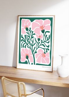 a pink and green flower print sitting on top of a wooden table next to a white vase