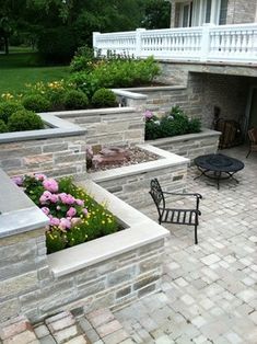 an outdoor patio with stone walls and seating area, surrounded by flowers and plants on the side