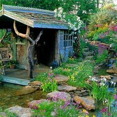 a garden with flowers, rocks and a small shed in the middle of it's yard