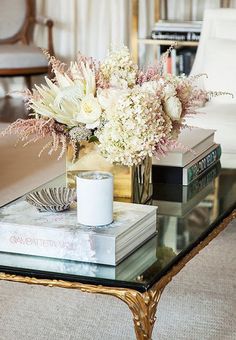 a coffee table with flowers and books on it, sitting in front of a couch