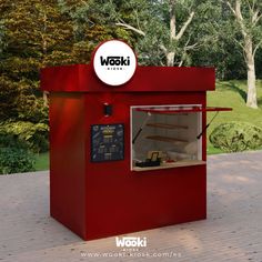 a red kiosk sitting on top of a wooden floor next to trees and grass