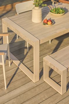 an outdoor table with two chairs and a bowl of fruit on it, sitting on a wooden deck