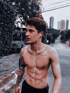 a shirtless man walking down the street with earphones in his ears and tattoos on his chest