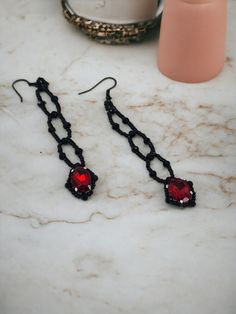 These elegant earrings, perfect for Victorian or gothic attire, features a striking design of black and deep red. It showcases one deep red oval crystal, hanging from delicate black seed beads, adding to its intricate allure. The earrings are 3 1/2" inches including the fish hook in length. This piece is both dramatic and sophisticated, making it an ideal accessory for those seeking to make a bold statement. The versatility of the gothic earrings knows no bounds. Whether you're preparing for a c Red Gothic Jewelry For Party, Handmade Gothic Plug Earrings As Gift, Handmade Edgy Plug Earrings As Gift, Edgy Red Earrings As Gift, Handmade Edgy Plug Earrings For Gift, Edgy Red Earrings For Gift, Edgy Red Earrings For Gifts, Red Gothic Earrings For Pierced Ears, Gothic Pierced Jewelry For Party