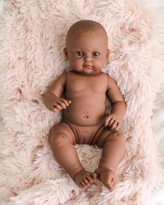 a baby doll sitting on top of a fluffy pink blanket