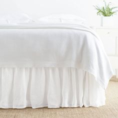 the bed is made with white linens and ruffled bedspread, along with a potted plant